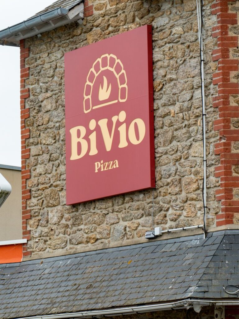 Enseigne extérieure rouge pour le restaurant BiVio Pizza sur un mur en pierre.
